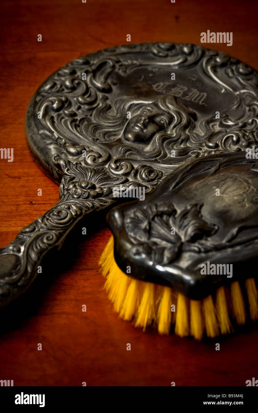 Still life of an antique brush and hand mirror with an ornate design of a woman with long locks of hair. Stock Photo