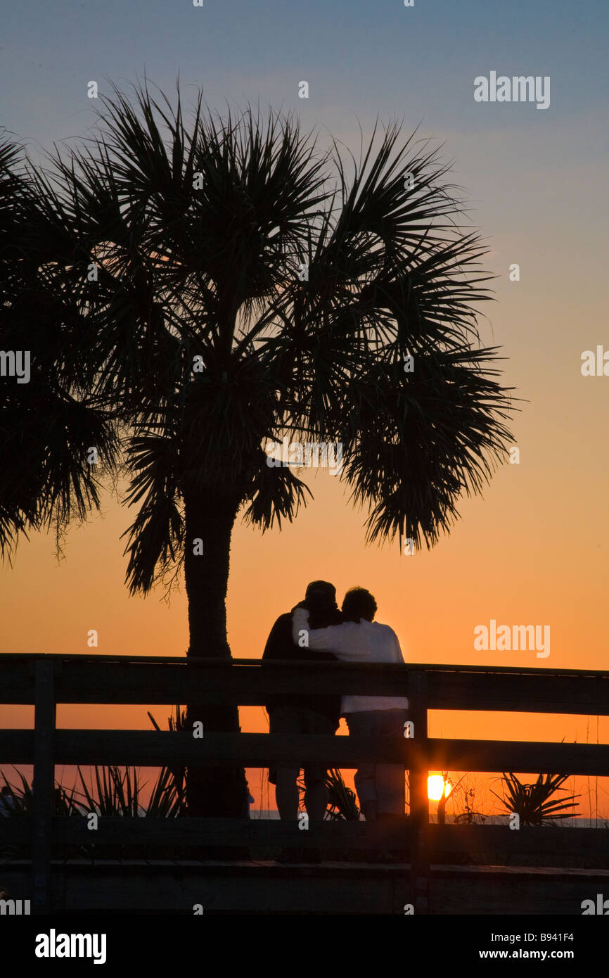 Silhouetted couple watching sunset under a palm tree at Nokomis Beach ...