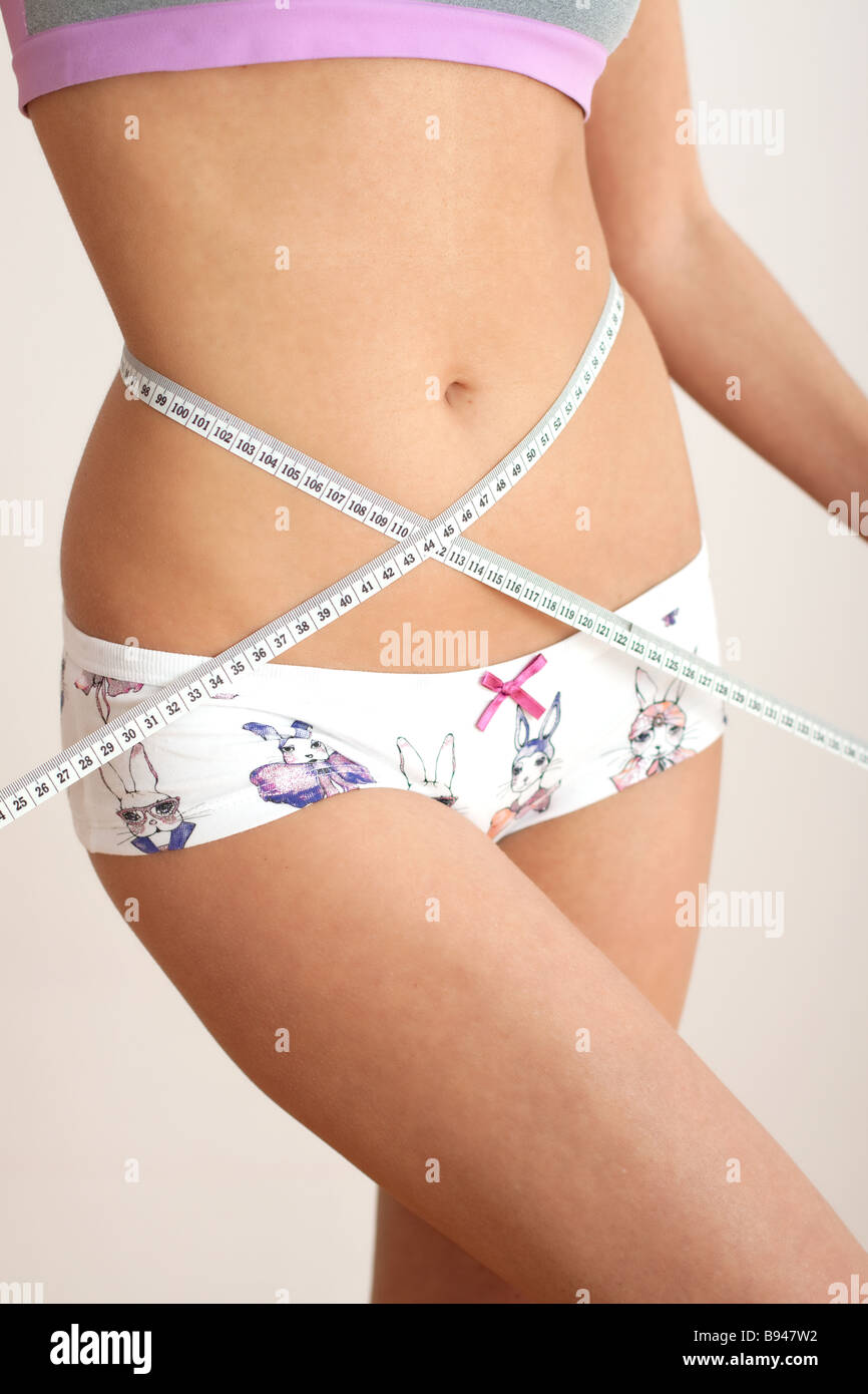 Young woman measuring waist with tape measure, close-up. Belly and navel. Stock Photo