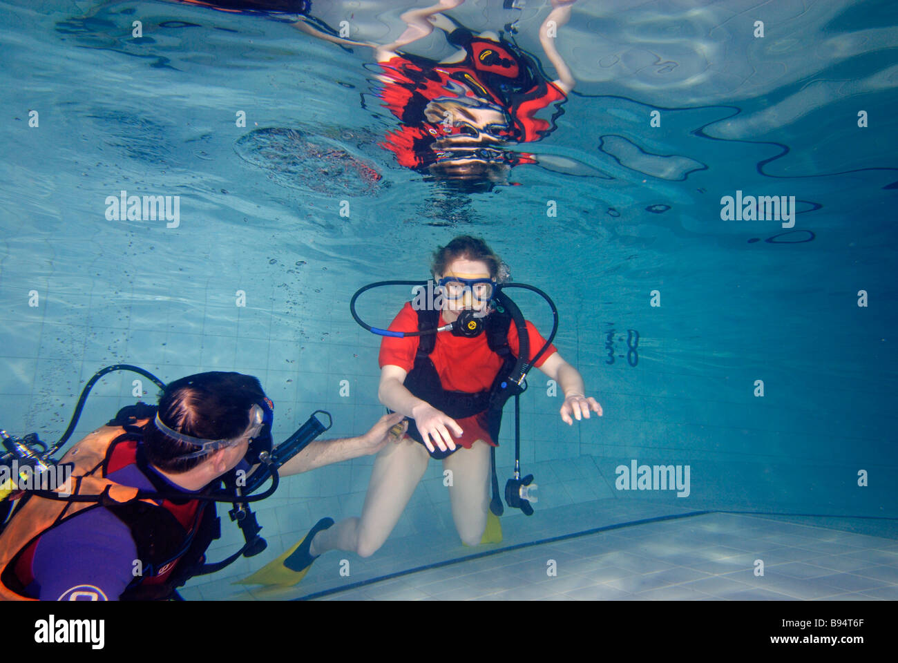 Young woman learning to scuba dive in pool with instructor teaching