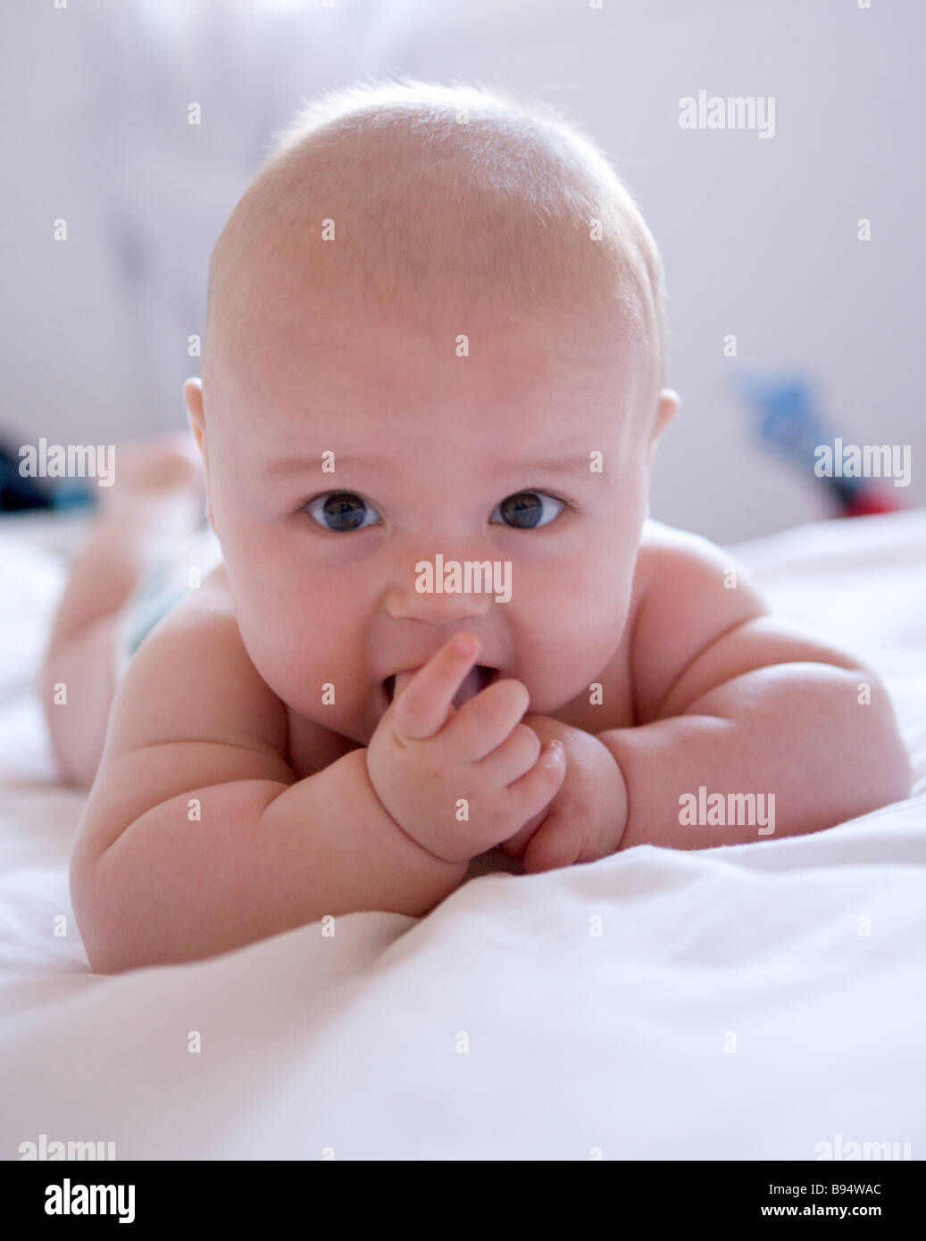 Small baby chuckling on a bed with window light behind him Stock Photo