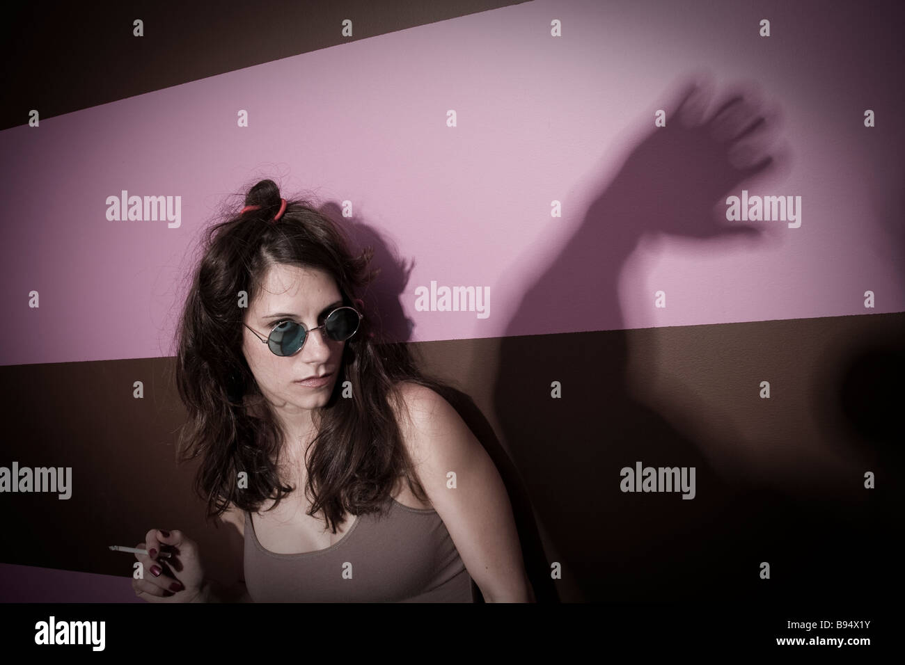 Young woman smoking a cigarette and wearing sunglasses in front of a shadow of a man s hand MODEL and LOCATION RELEASED Stock Photo