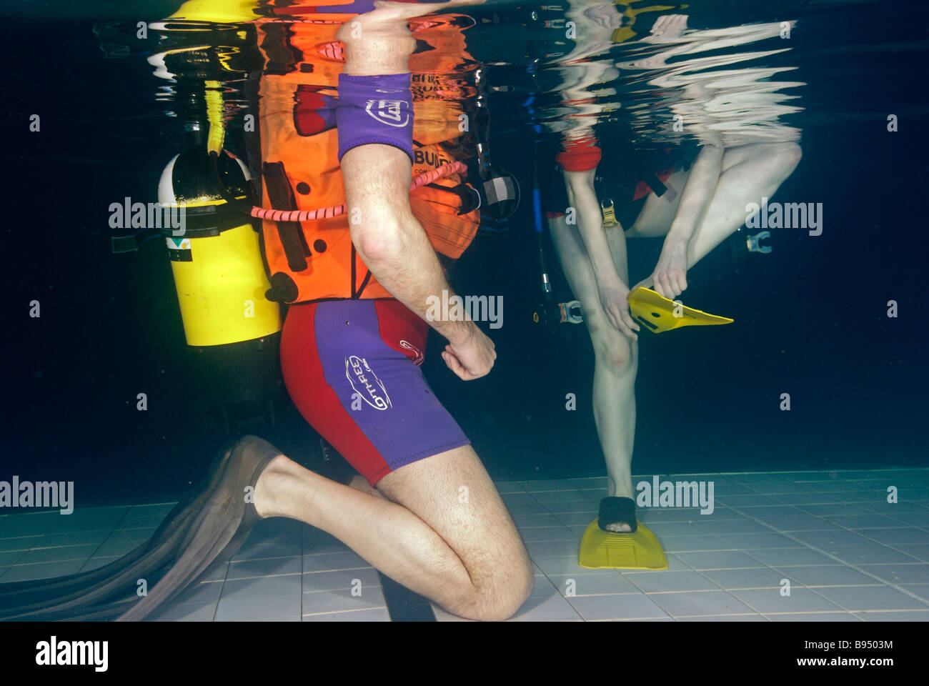 Young woman learning to scuba dive standing in pool putting fins on