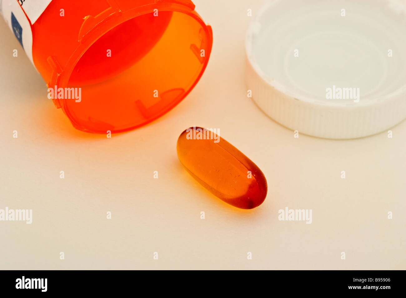 Single clear medicine capsule in front of an open empty prescription bottle and cap Stock Photo