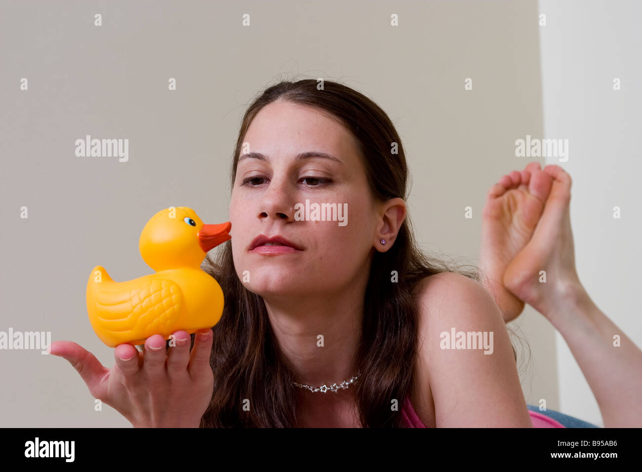 Young woman holding a rubber duck lying on her bed MODEL RELEASED Stock Photo