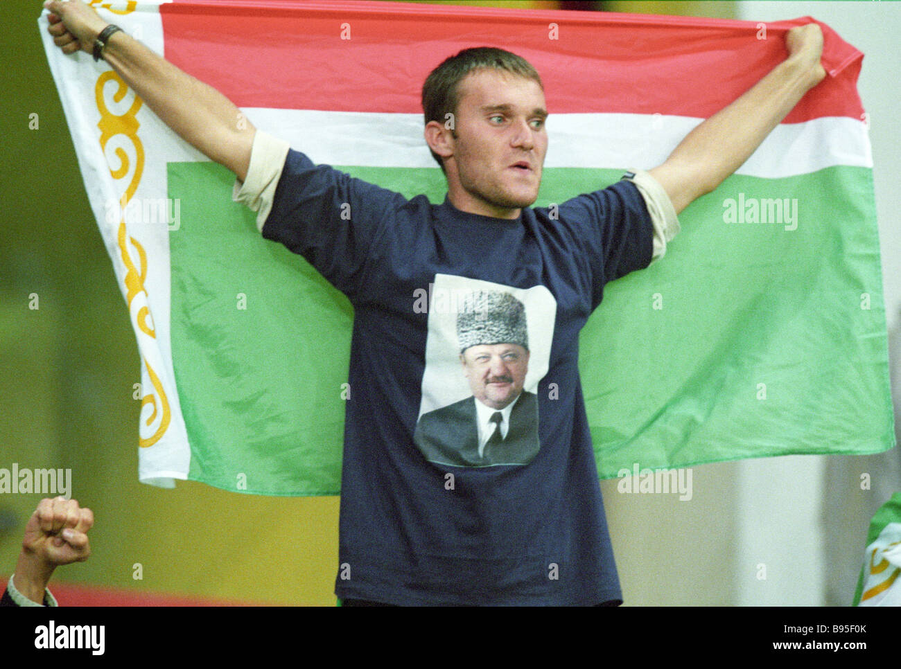 A Chechen fan in a T shirt with an image of Akhmad Kadyrov on it waving a  Chechen flag The Grozny football team Terek and the Stock Photo - Alamy