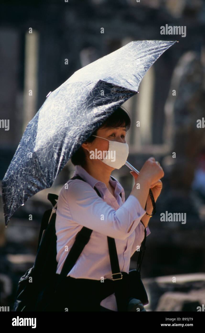 Cambodia Siem Reap Province Angkor Wat Thom Japanese Tourist At Bayon Temple Wearing Face Mask And Holding An Umbrella For Shade Stock Photo