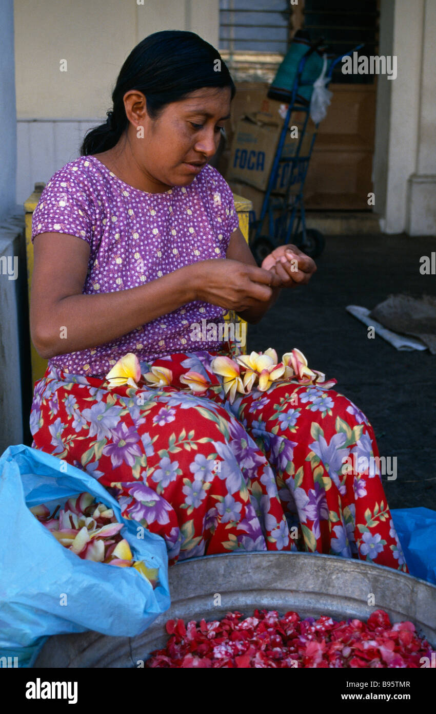 MEXICO Juchitan Woman in floral patterned skirt threading flower heads into garland at Juchitan street market. Stock Photo