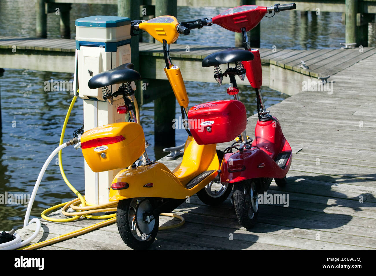 Two alternative energy vehicles, electric scooters on a dock at lakeside. Stock Photo