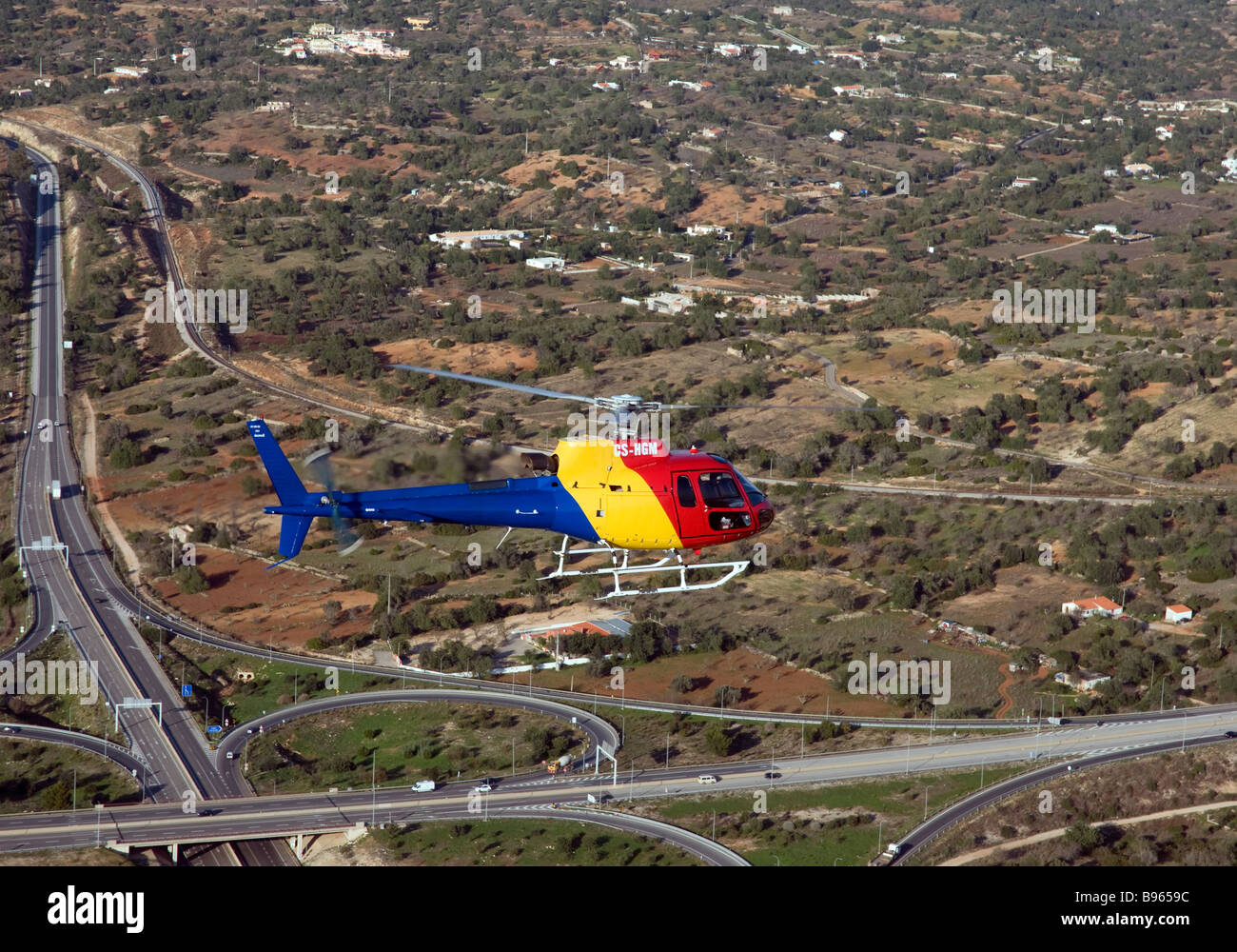 A multipurpose helicopter in colourful livery flies over the A22 motorway and a railway line in the Algarve, southern Portugal Stock Photo