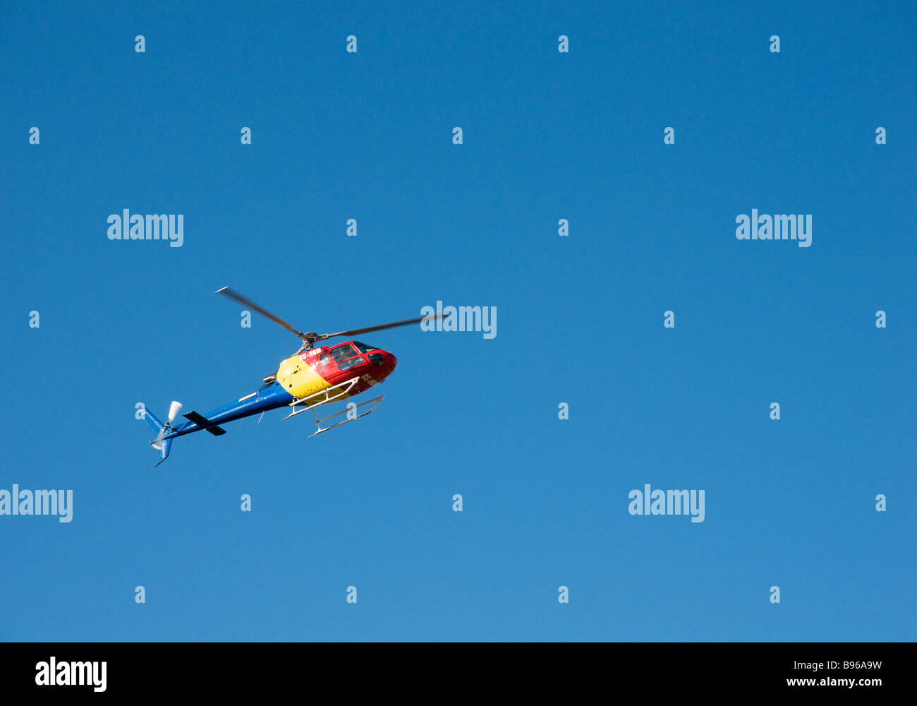 A multipurpose helicopter in colourful livery hovers under a clear blue sky Stock Photo