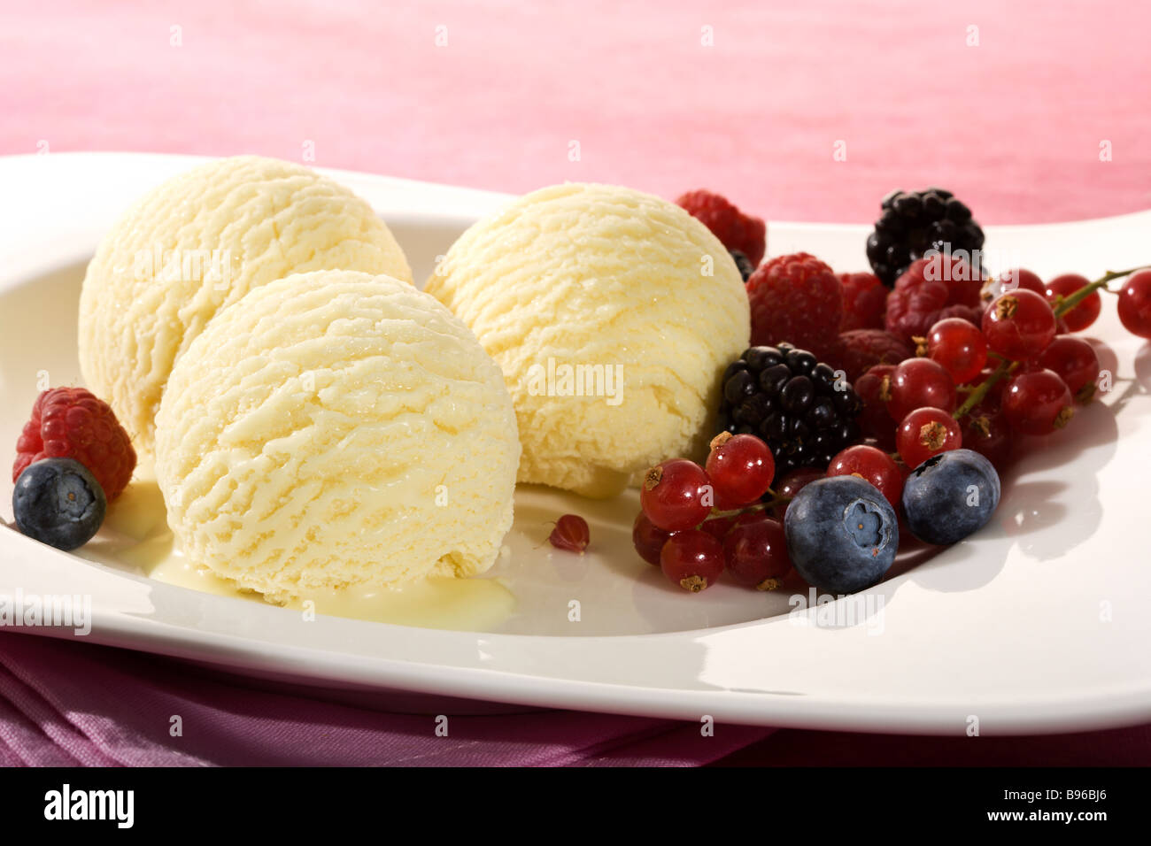 close up of three scoops of vanilla icecream arranged with various berry fruit on white plate Stock Photo