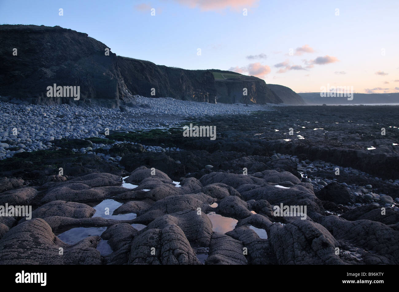 Pebble beach in Devon, cliffs in background, rockpools in foreground Stock Photo