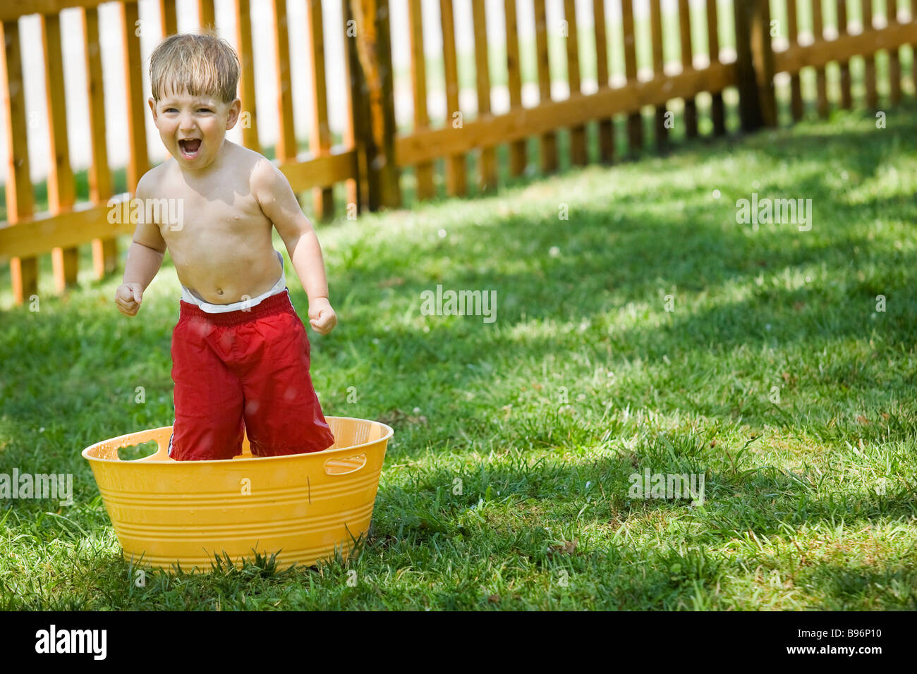 A two year old boy screams with joy while soaking in a yellow tub of
