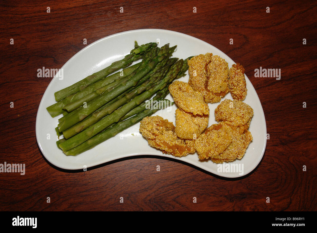 still life of a boomerang shaped plate of bacalaitos cod fish fritters and asparagus on a wood table viewed from above Stock Photo