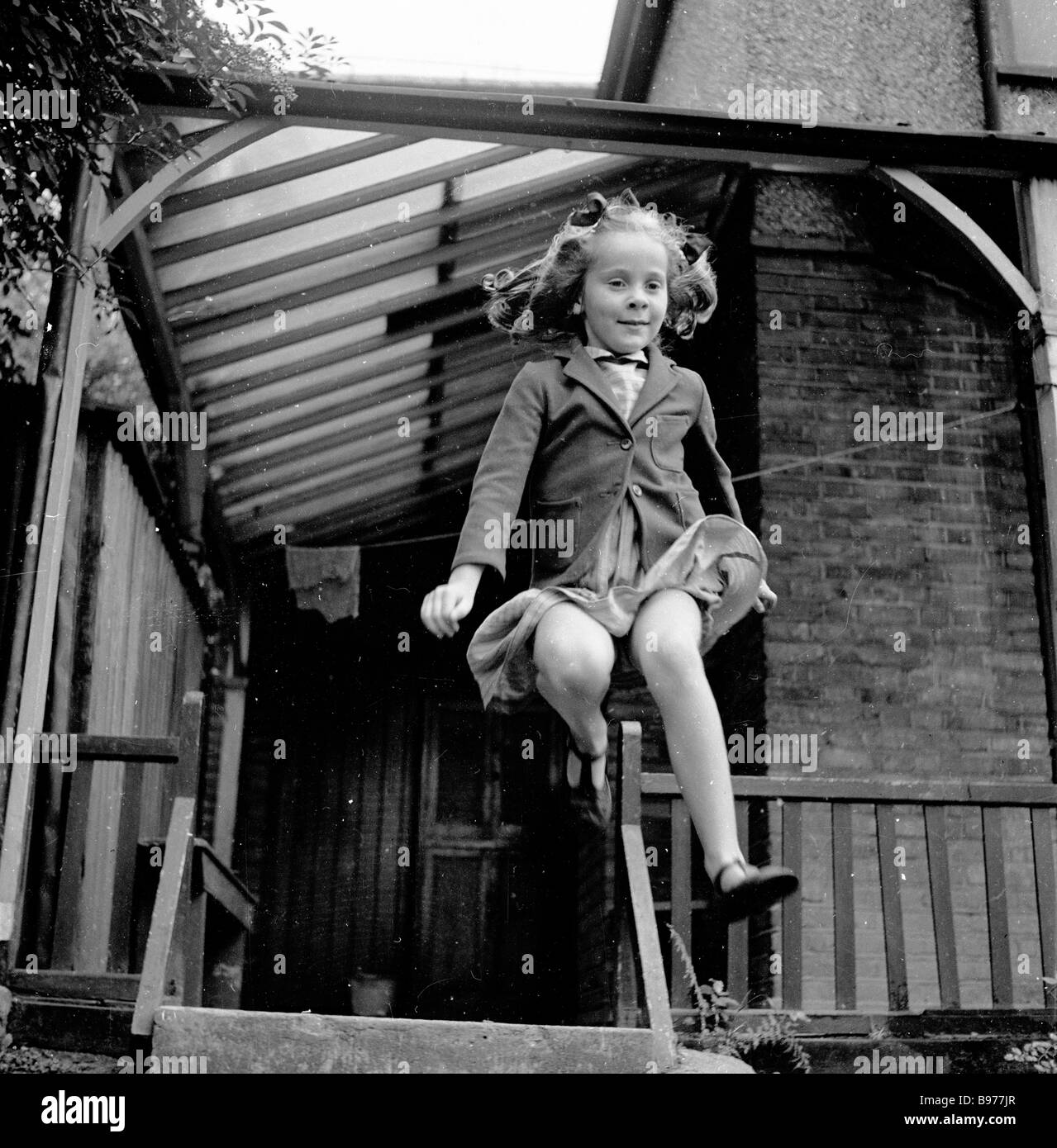 1950s, a young schoolgirl jumping from the back veranda or side porch of a house, London England,UK, in this historical picture by J Allan Cash. Stock Photo
