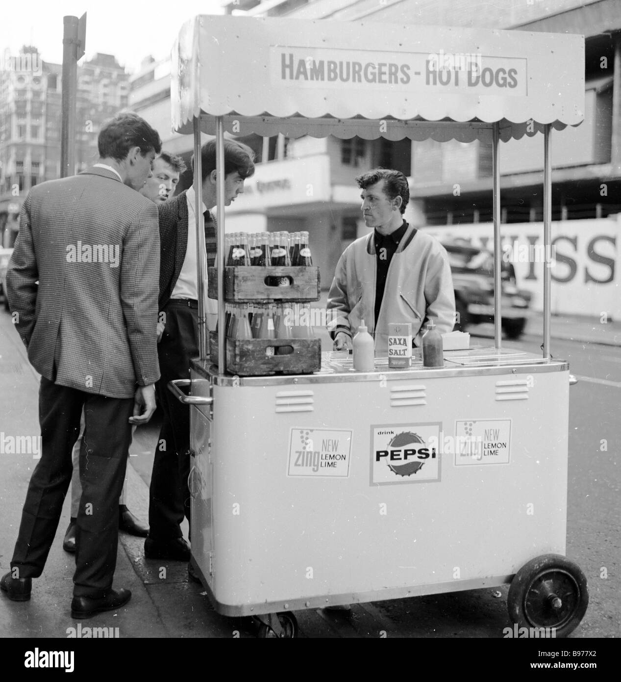 1950s, suited young men check what food and drink are available from a small snack or fast food street vendor in Wardour Street, London, England, UK. Stock Photo
