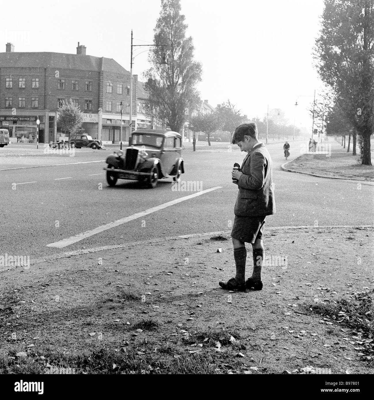 1950s, historical, a schoolboy standing on a corner of a street taking pictures of moving cars with his Kodak Brownie film camera, England, UK. Stock Photo