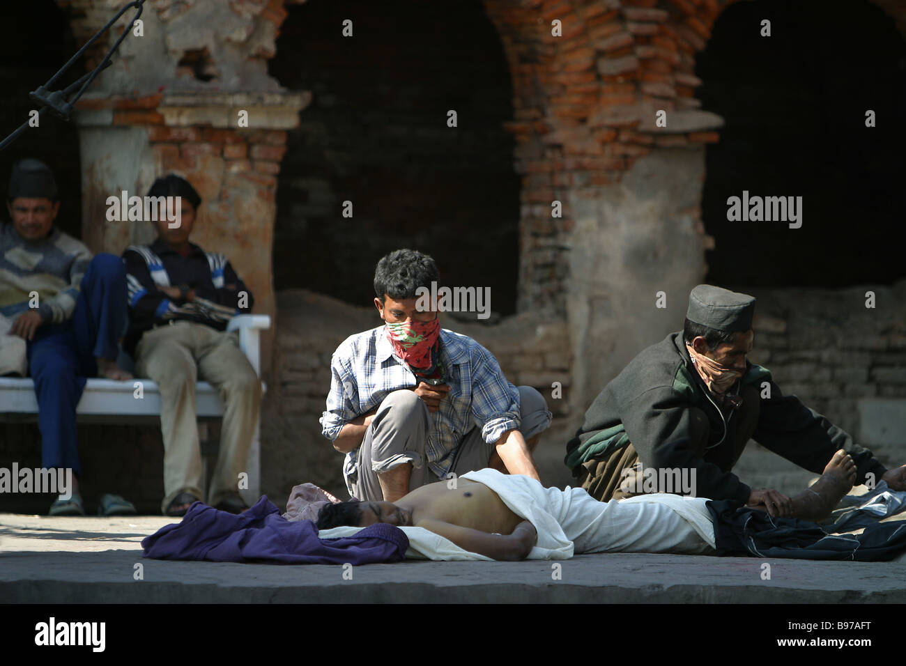 Men prepare a dead body for cremation on a funeral wood pire at the