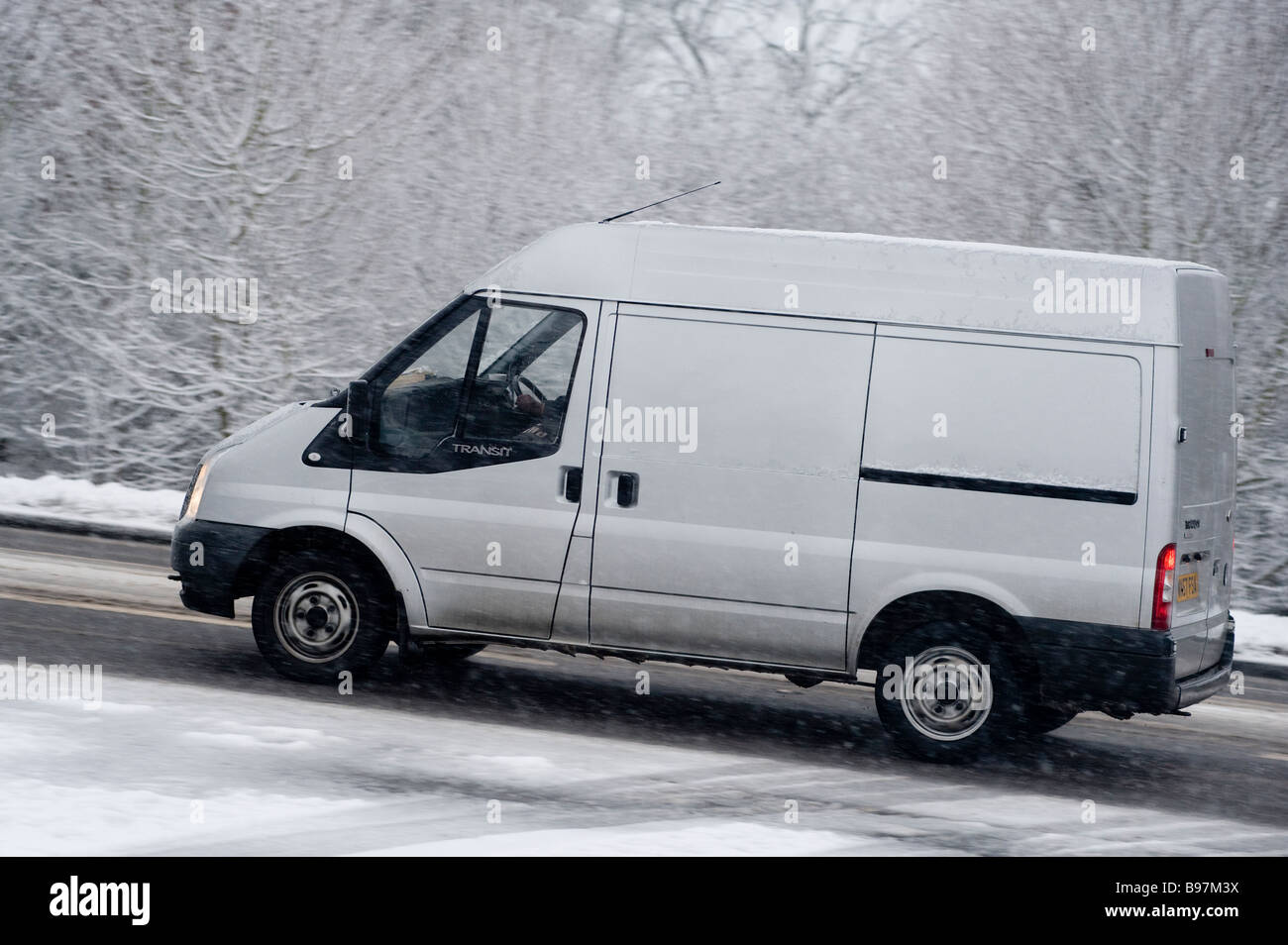 Side view of a transit van driving along a snow covered road on a winters day in England. Stock Photo