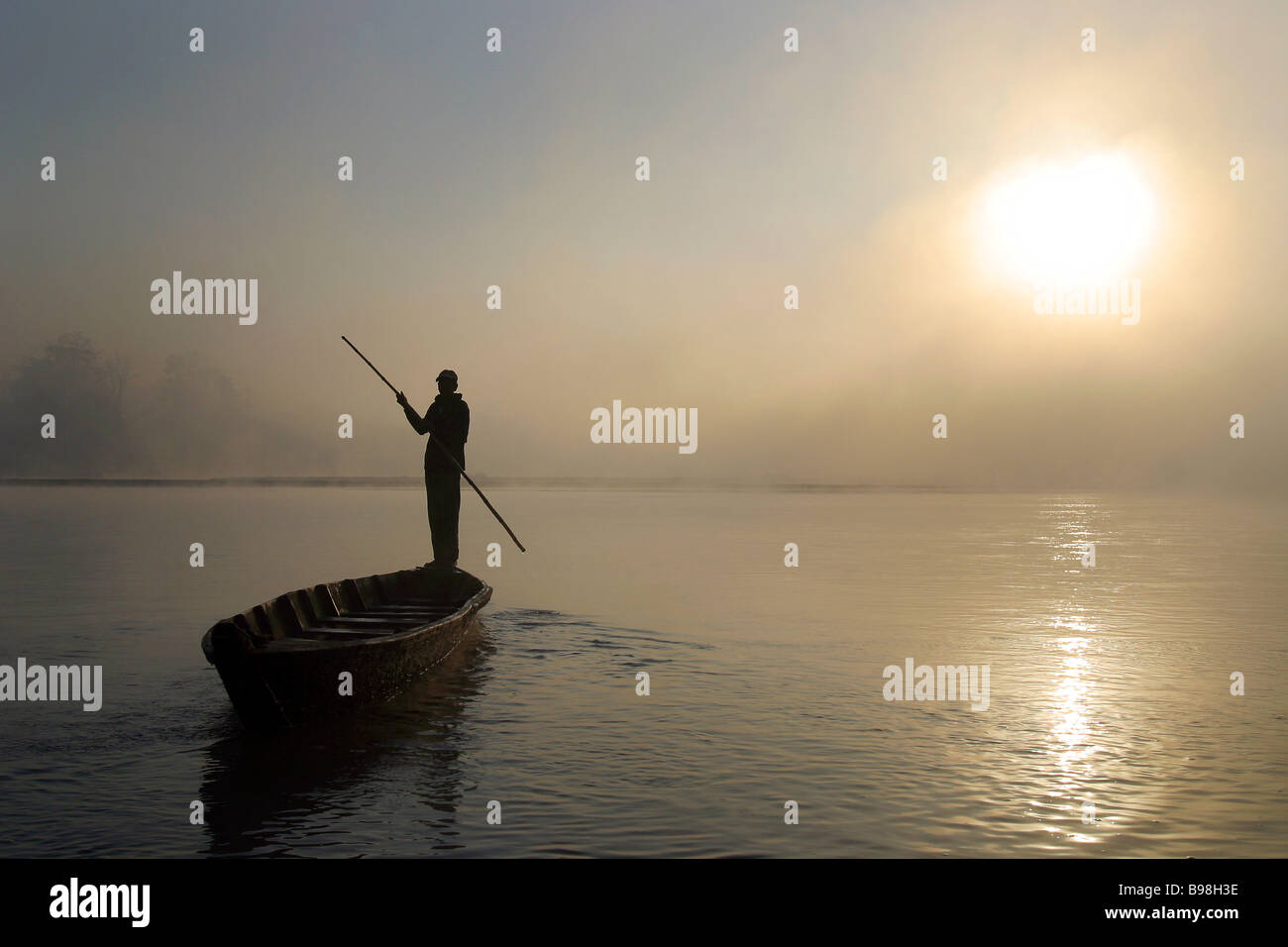 A man stands in a canoe in the morning mist along the Rapti River bordering Chitwan National Park in Sauraha, Nepal. Stock Photo