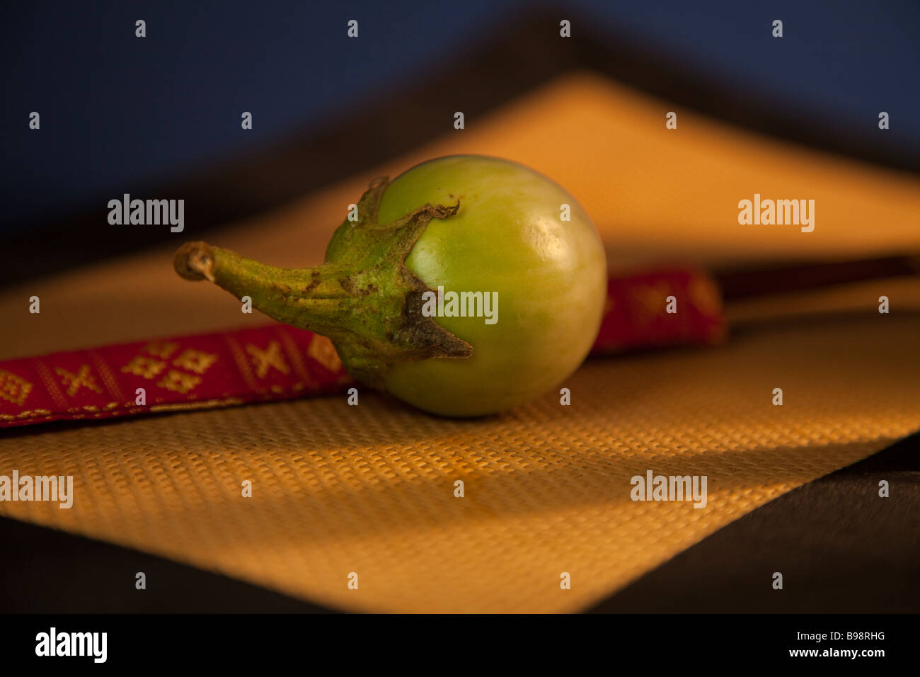 Thai aubergine or egg plant on placemat with coloured silk chopstick holder in background lit warm light Stock Photo