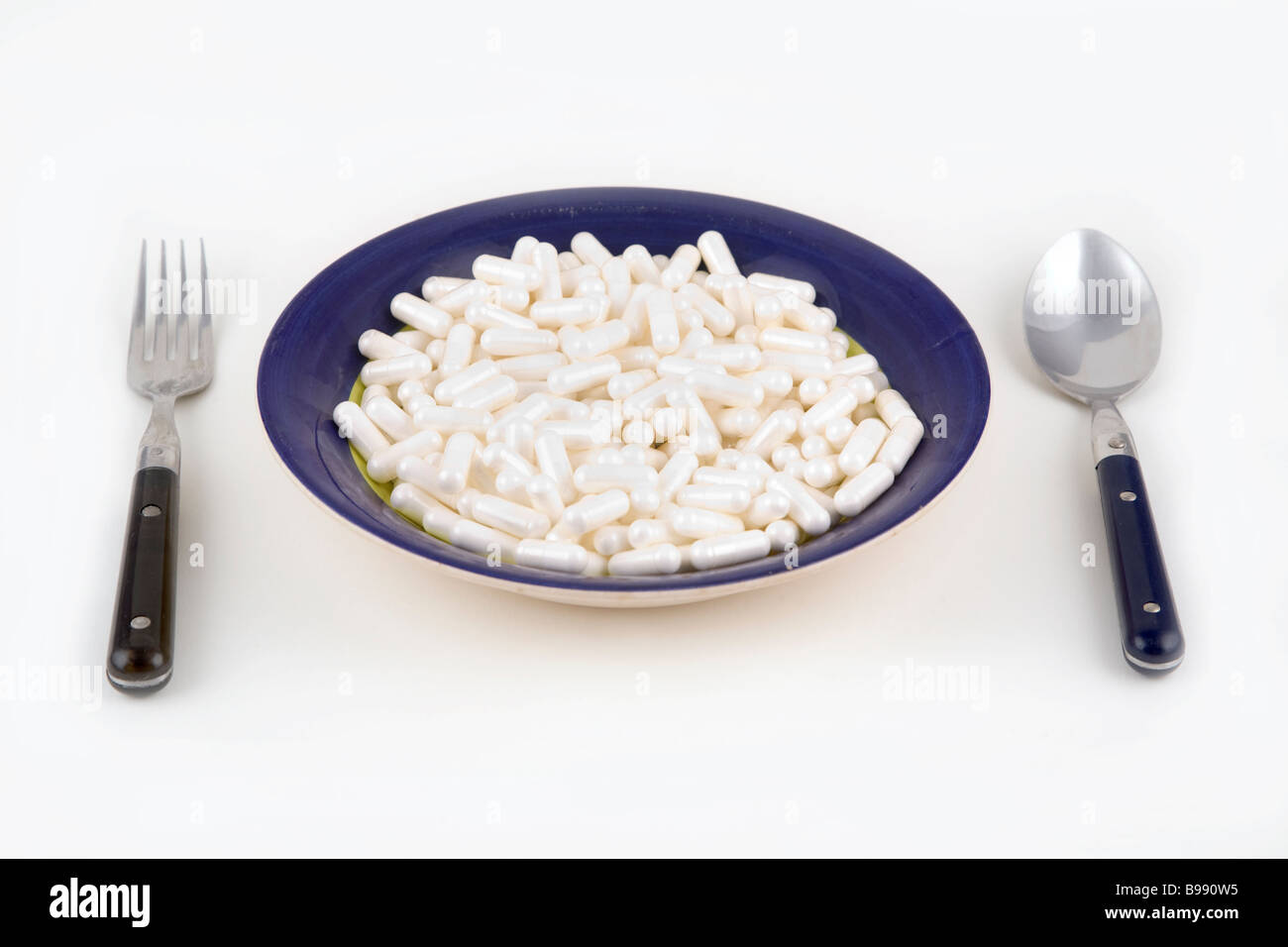 A bowl of pills with a knife and spoon on a white background Stock Photo