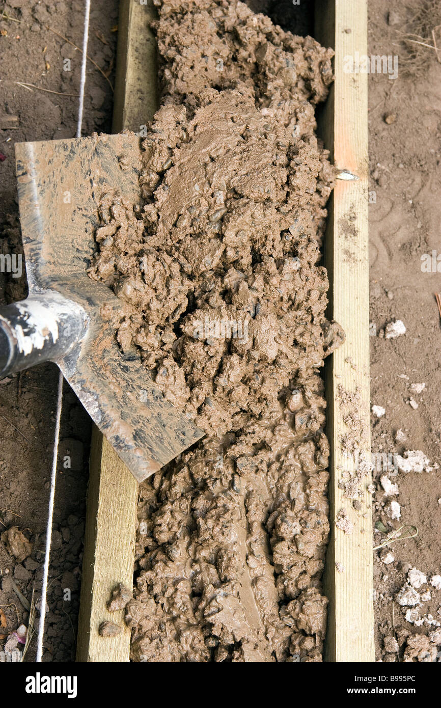 A spade full of concrete is shovelled into the shuttering ready to form the footings for a small garden wall Stock Photo