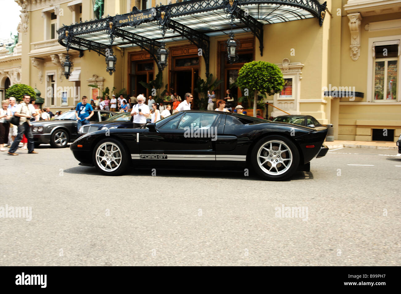 A black Ford GT 40 drives by the Hotel de Paris in Monaco Monte Carlo with tourists looking at Stock Photo