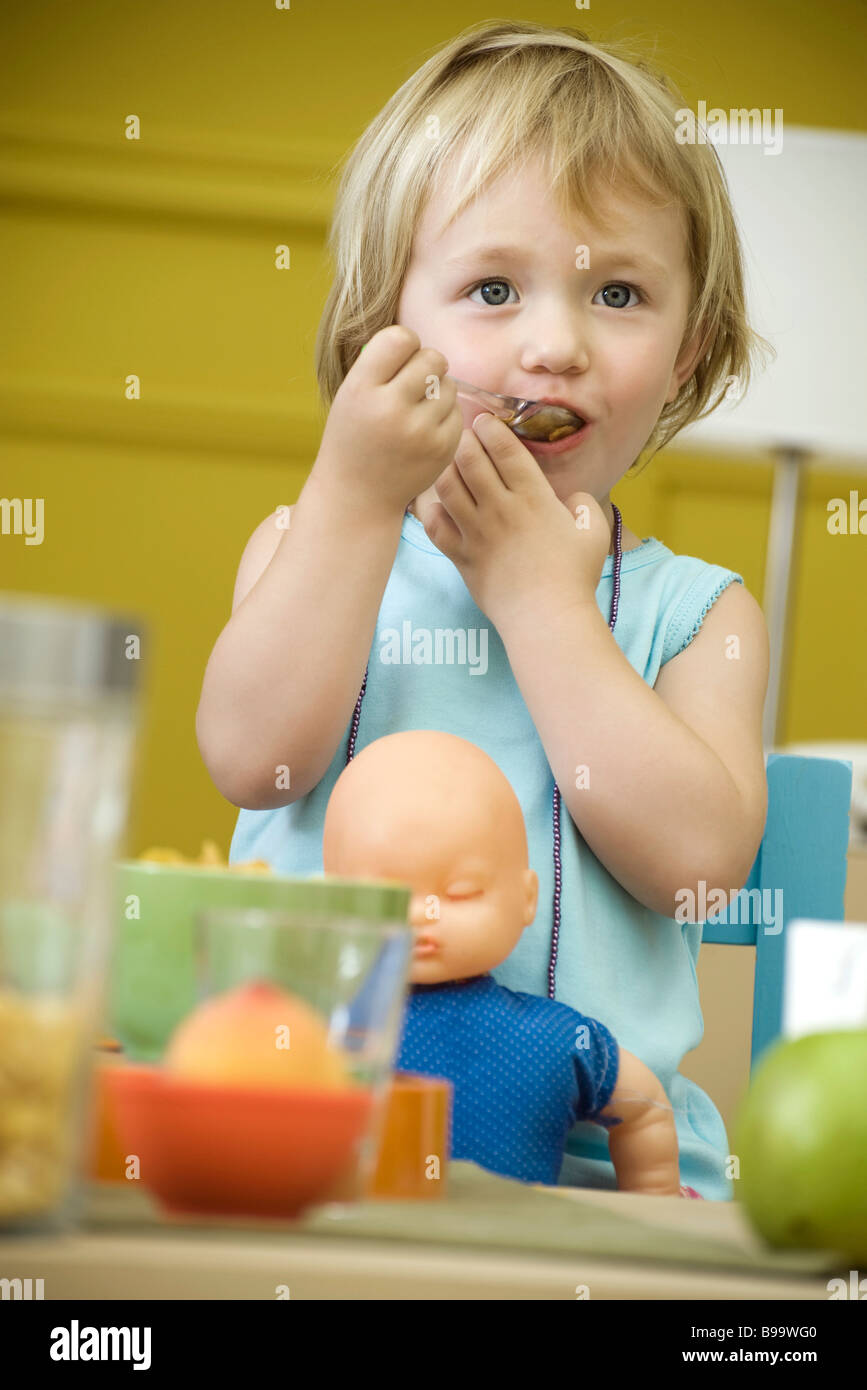 Toddler girl eating at table, baby doll in lap Stock Photo Alamy