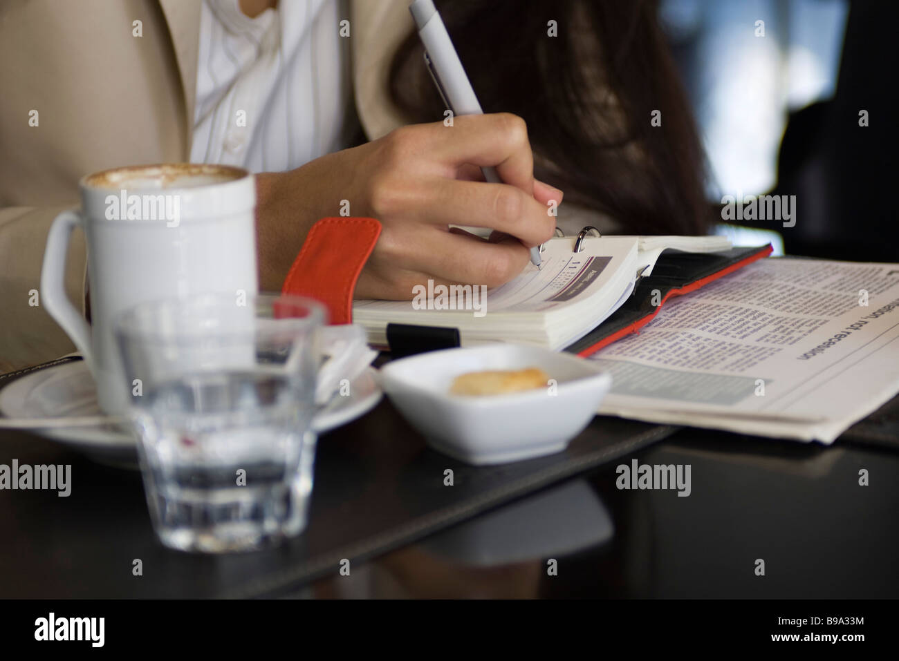 Woman sitting in cafe, writing in agenda, cropped view Stock Photo