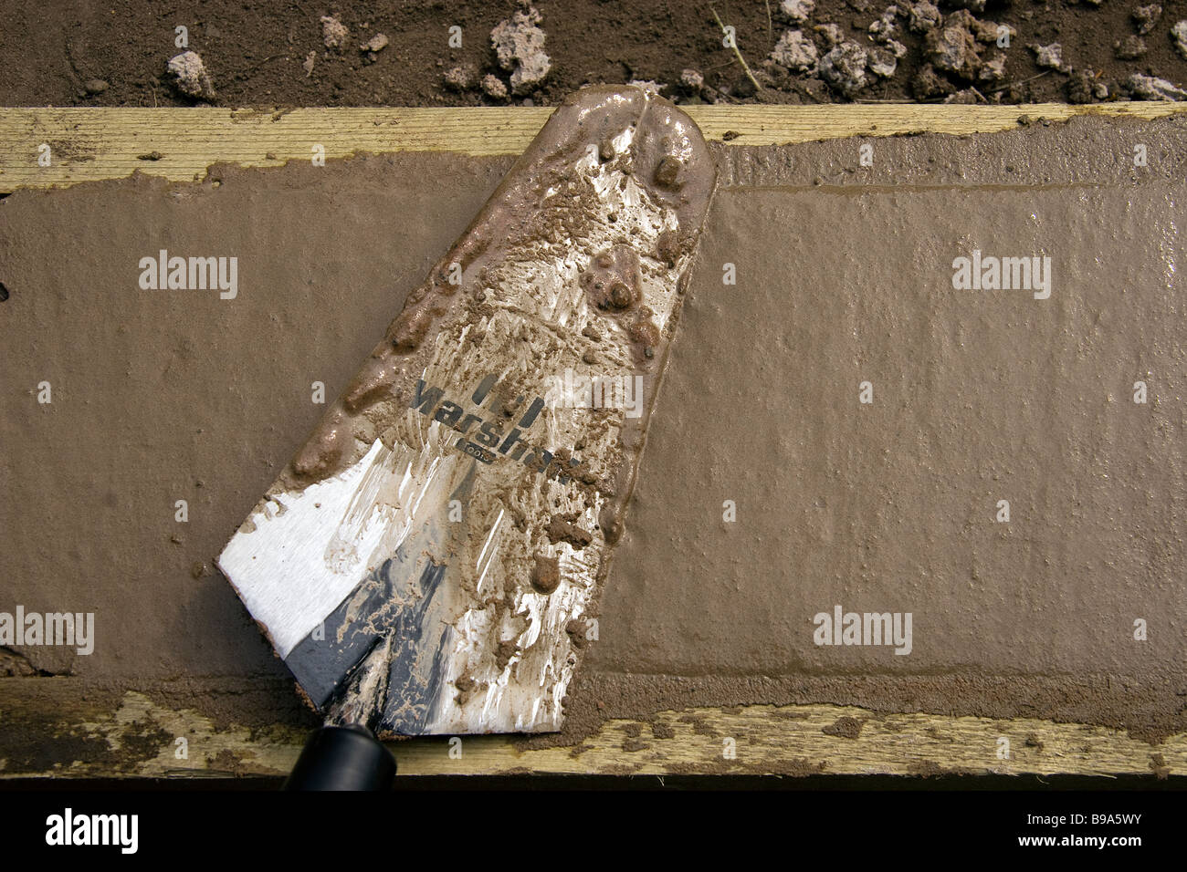 A trowel is used to float the level of concrete footings of a small garden wall between two lengths of 2 by 1 used as shuttering Stock Photo