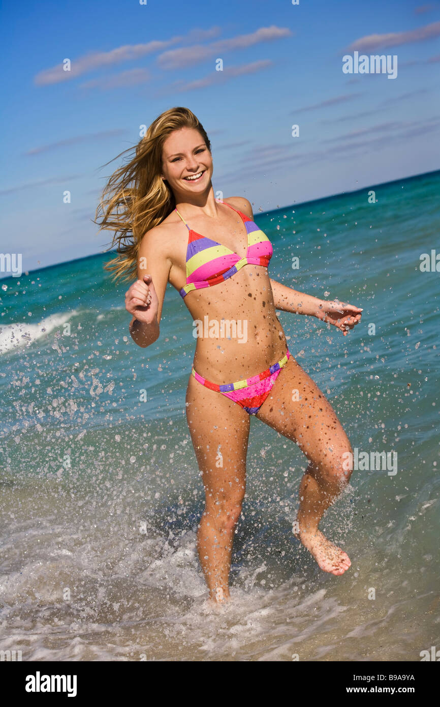 Beautiful Caucasian female teenager running through to surf wearing a  colorful bikini Stock Photo - Alamy