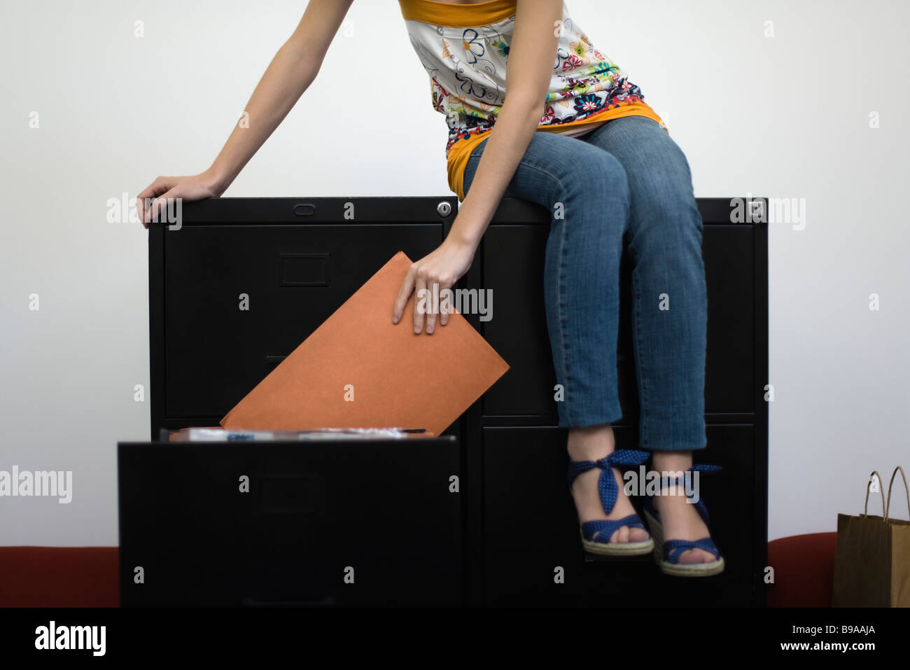 Woman sitting on filling cabinets, removing file from drawer, cropped Stock Photo
