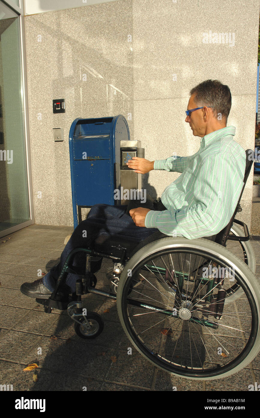 full length profile side view urban portrait of a handicapped man in a wheelchair using an automatic automated door copy space Stock Photo