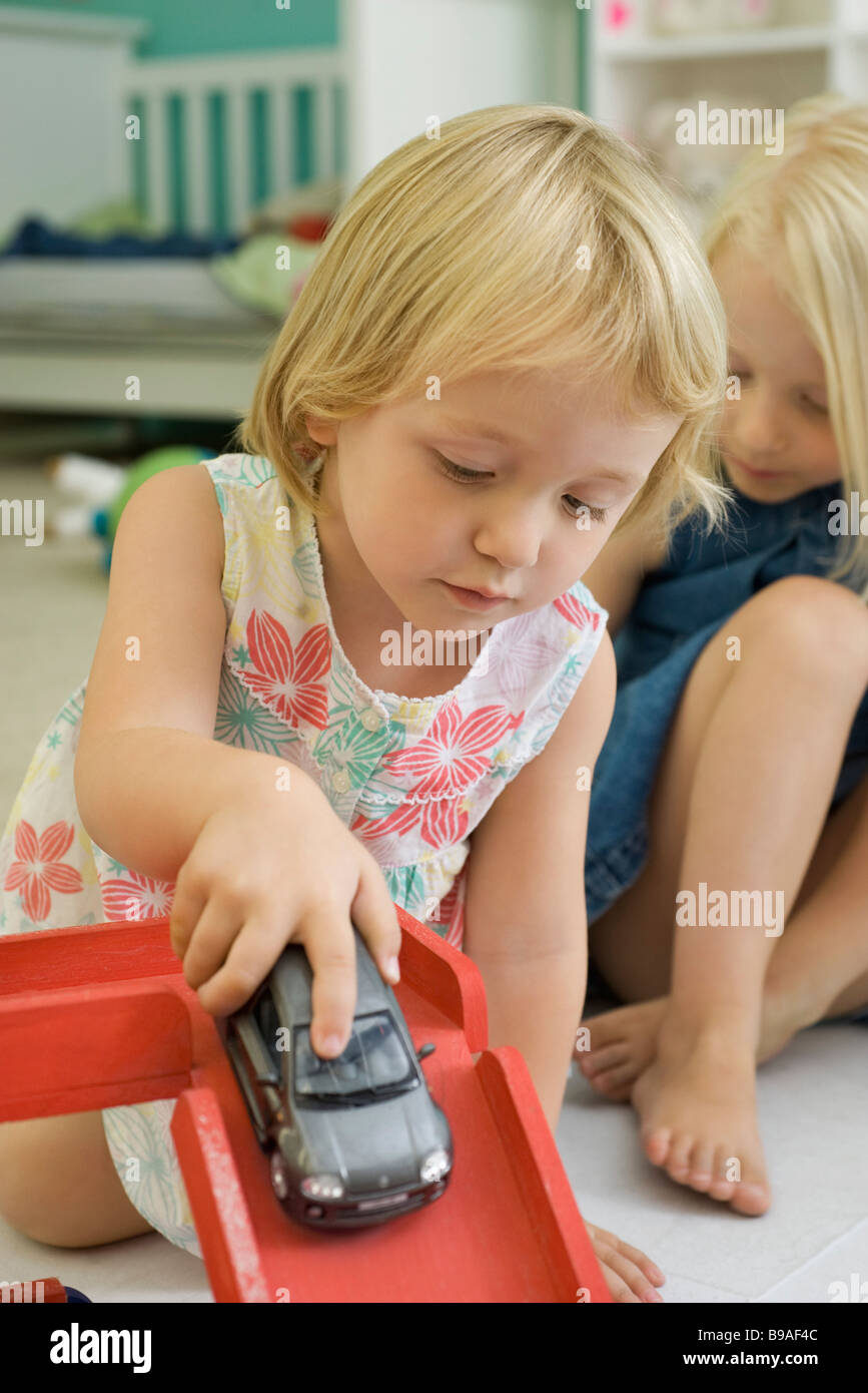 Little girl playing with toy car, sister in background Stock Photo