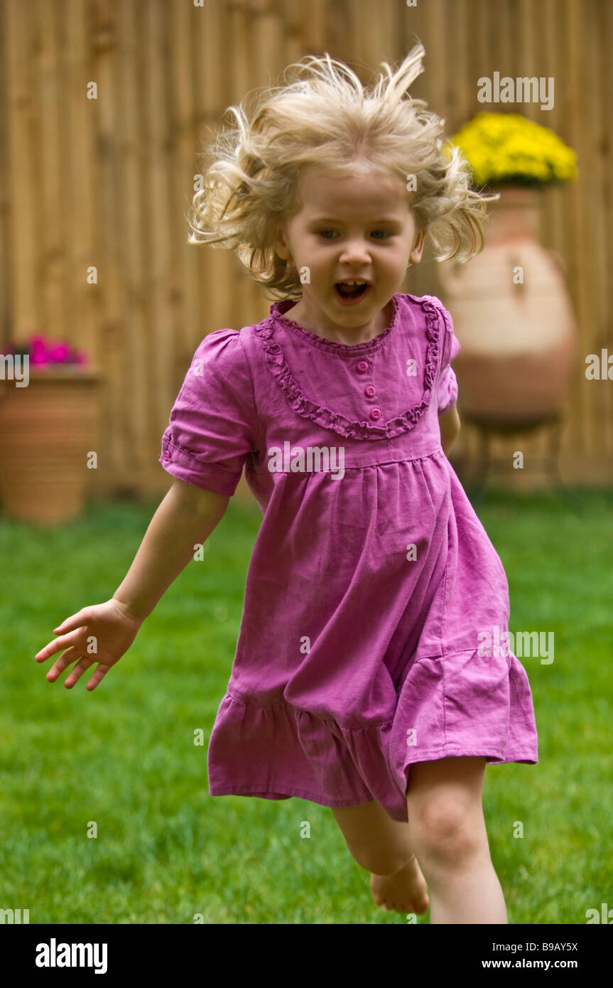 young 3 three year old girl running and smiling in garden spring summer time Stock Photo