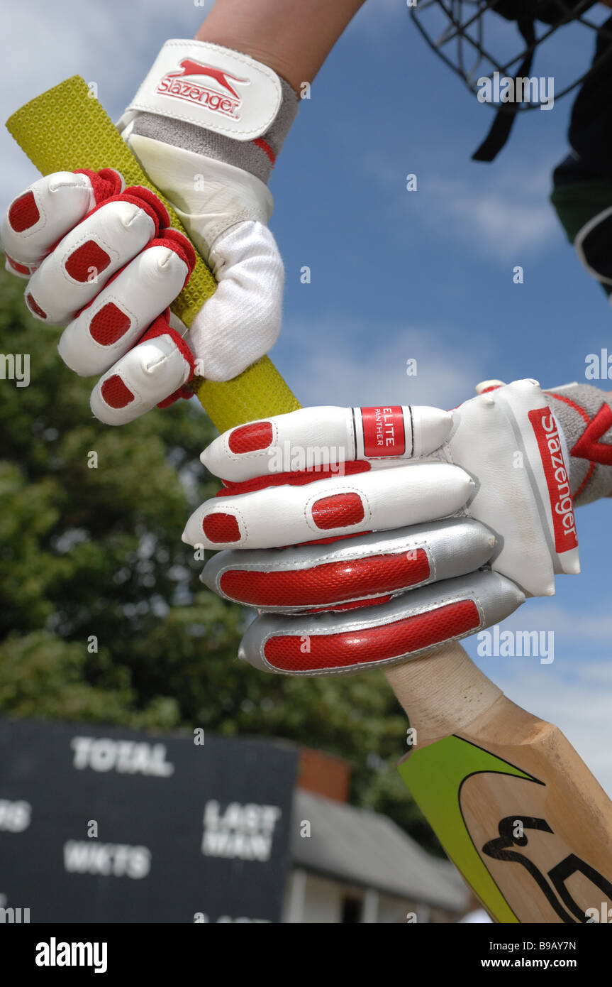 Closeup of a pair of hands holding a cricket bat on a sunny day with the scoreboard in the background Stock Photo