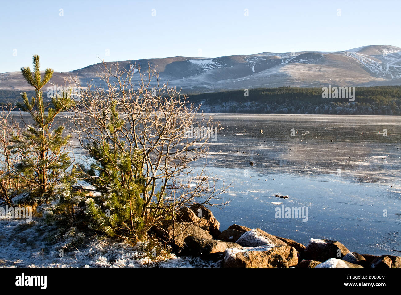 Ice on Loch Morlich near the Cairngorm mountains in the highlands of Scotland with snowy moutains in the background Stock Photo