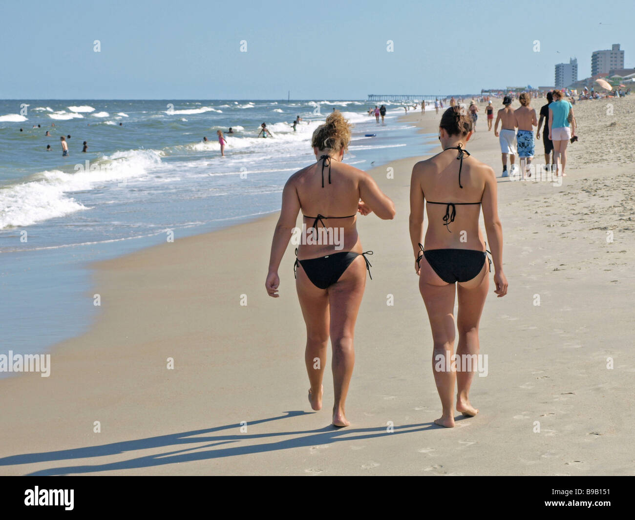 two girls in bikinis walking on Atlantic Ocean beach with people ahead no faces blue sky summer Stock Photo