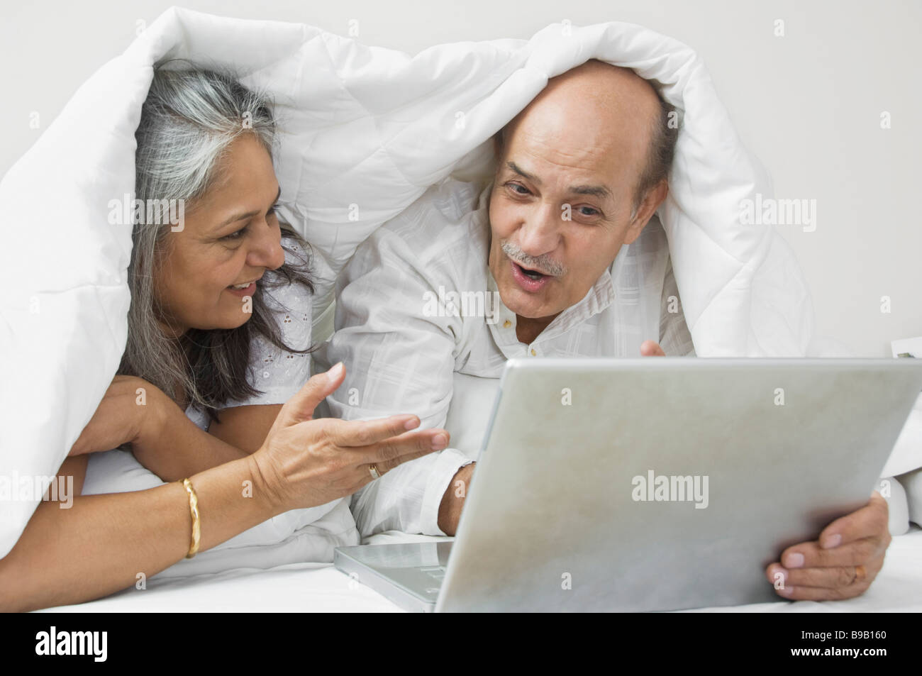 Couple using a laptop on the bed and smiling Stock Photo - Alamy