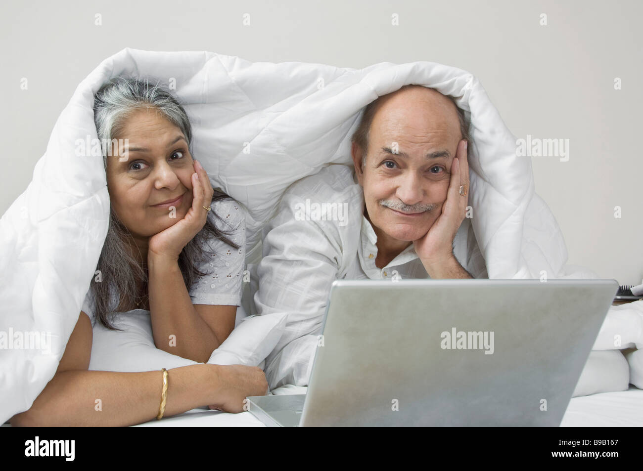Couple using a laptop on the bed and smiling Stock Photo - Alamy