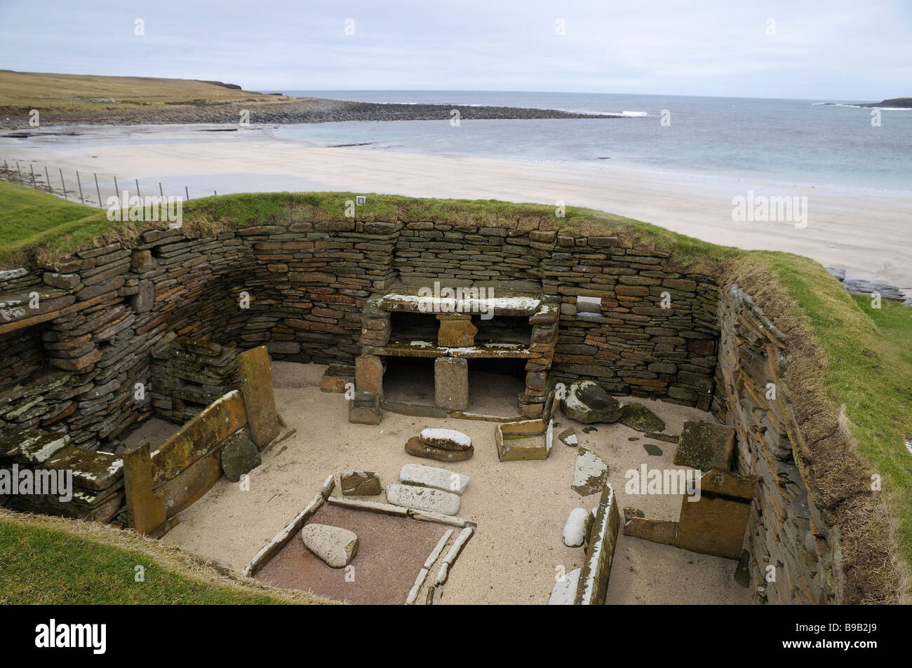 One of the ancient roundhouses excavated at Skara Brae, Orkney, Scotland, with beach and sea in background. Stock Photo