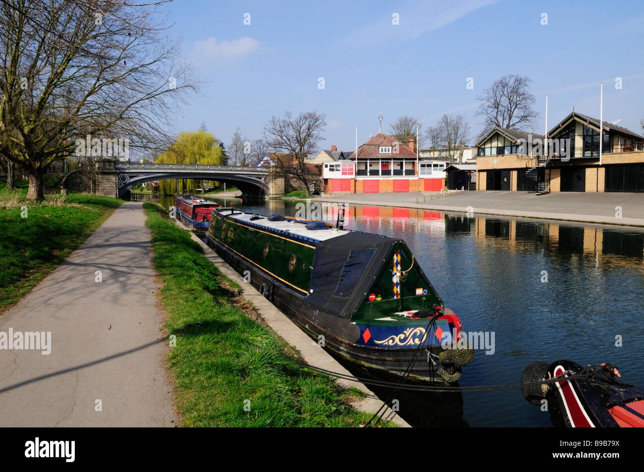 Narrowboats moored on the River Cam at Midsummer Common, with rowing boathouses on the far bank,  Cambridge England UK Stock Photo