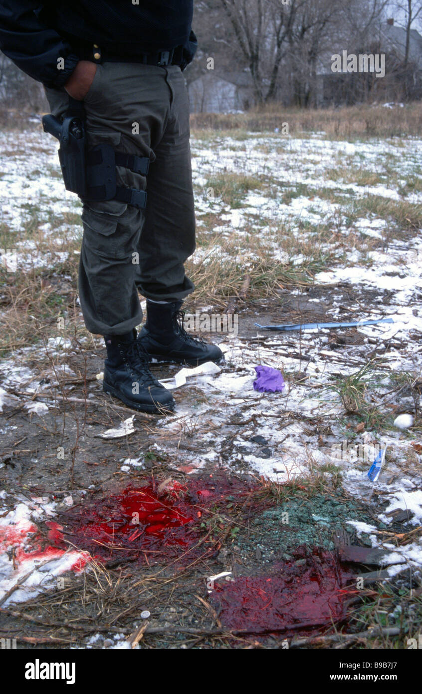 Cop standing by a pool of blood at a murder scene of a gangland execution in Detroit Michigan USA Stock Photo