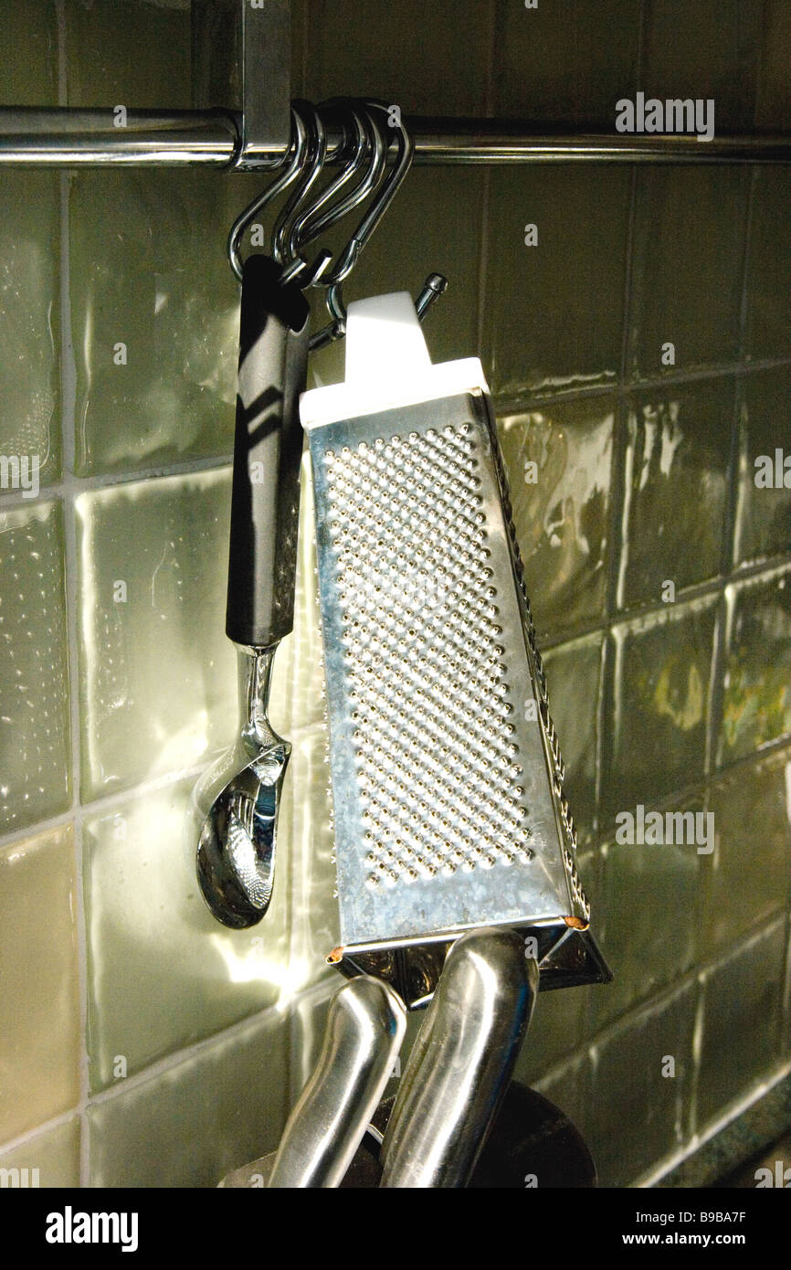 Grater and scoop hanging on tiled kitchen wall Stock Photo