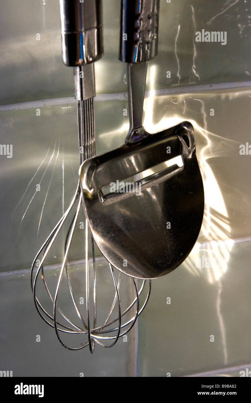 https://c8.alamy.com/comp/B9BA82/cheese-slicer-parer-and-whisk-hanging-on-tiled-kitchen-wall-B9BA82.jpg