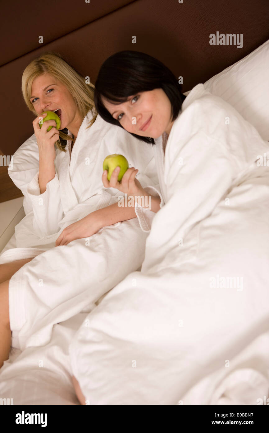 zwei fraun liegen apfel esend im bett und entspannen, lachen, sind entspannt Stock Photo
