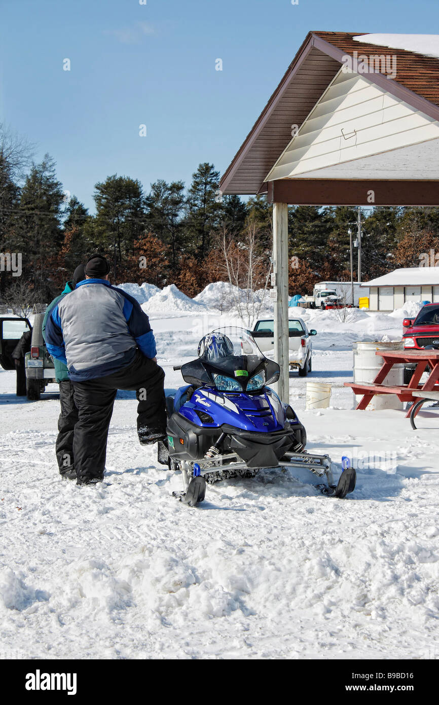 A young man with a snowmobile parked in a small town on the street in USA US lifestyle daily life drifts a lot of snow hi-res Stock Photo