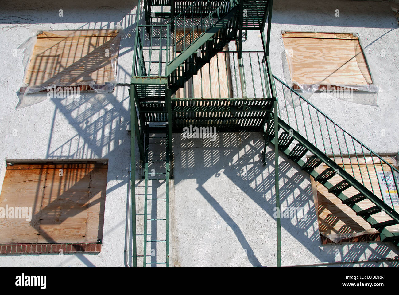 A green fire escape on the side of a boarded up and abandoned former luxury hotel building. Stock Photo